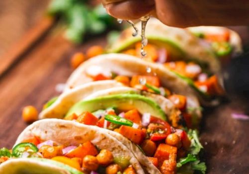 A hand squeezes lime over chickpea and vegetable tacos garnished with cilantro, on a wooden board with lime slices.