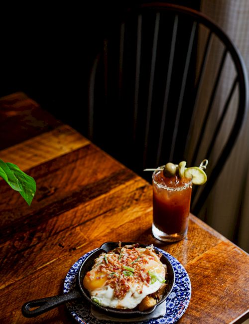 A sunny-side egg over toast served on a blue plate, with an iced drink garnished with fruit on a wooden table.