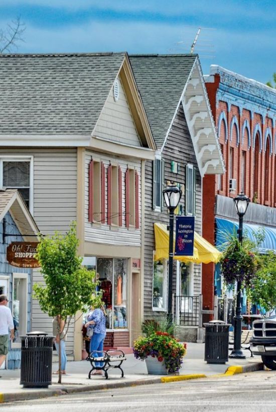 A quaint street with colorful storefronts, a street lamp, and potted plants. People are walking and a banner reads "Historic Lexington."