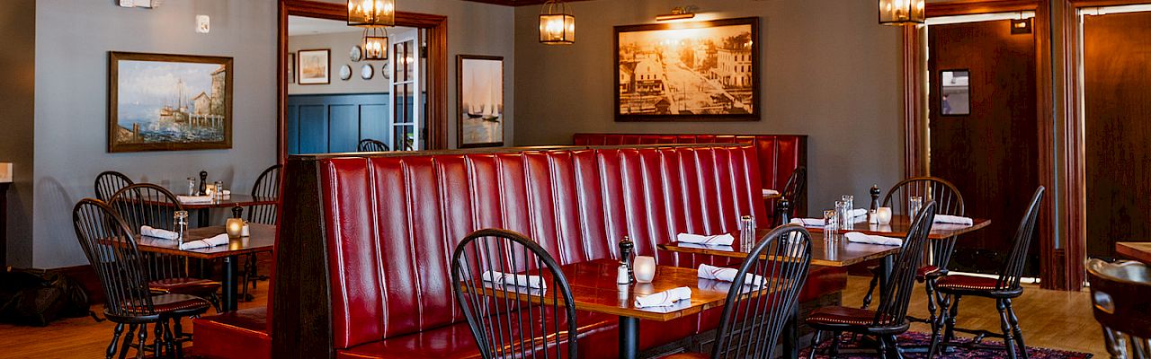 Warm restaurant dining room with red leather booth seating, wooden tables, and hanging lantern-style chandeliers.