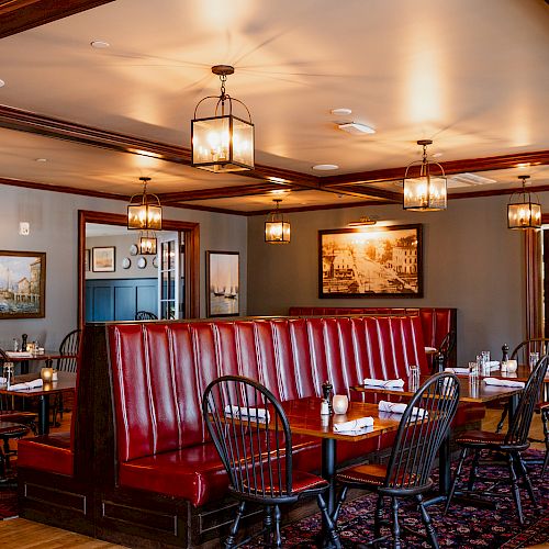 Warm restaurant dining room with red leather booth seating, wooden tables, and hanging lantern-style chandeliers.