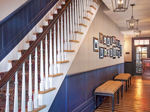 A staircase with a patterned carpet, framed photos on the wall, wooden benches, and hanging lanterns in a hallway.