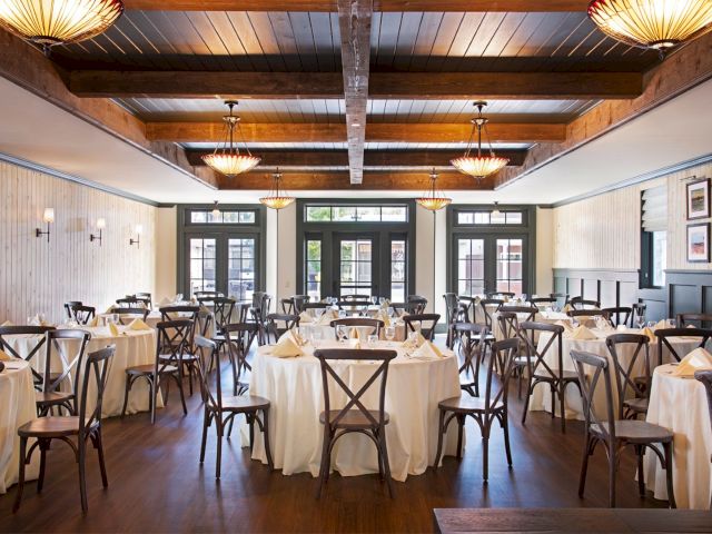 This image shows a stylish, empty restaurant with elegantly set tables, wooden chairs, and ambient lighting from ceiling fixtures.
