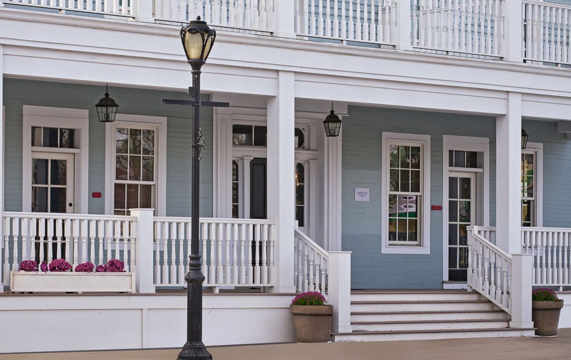 The image shows a light blue, three-story building with white trim and a balcony, set in a small, picturesque town.