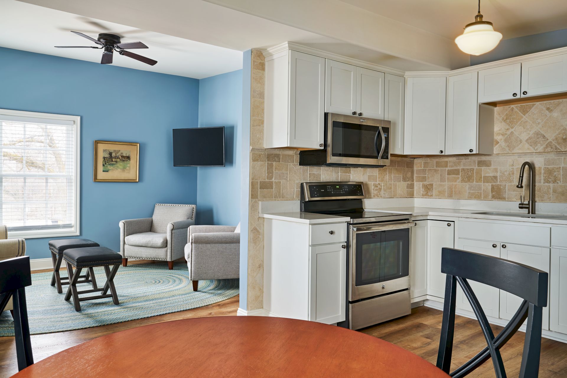 A kitchen and living area feature white cabinets, stainless steel appliances, and blue walls with chairs and a TV.