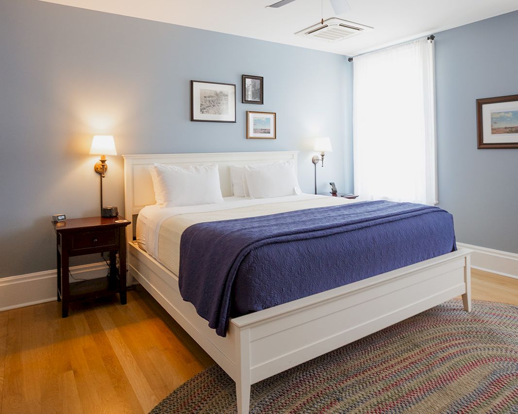 A tidy bedroom with a white bed, bedside lamps, a patterned rug, and a ceiling fan above it.